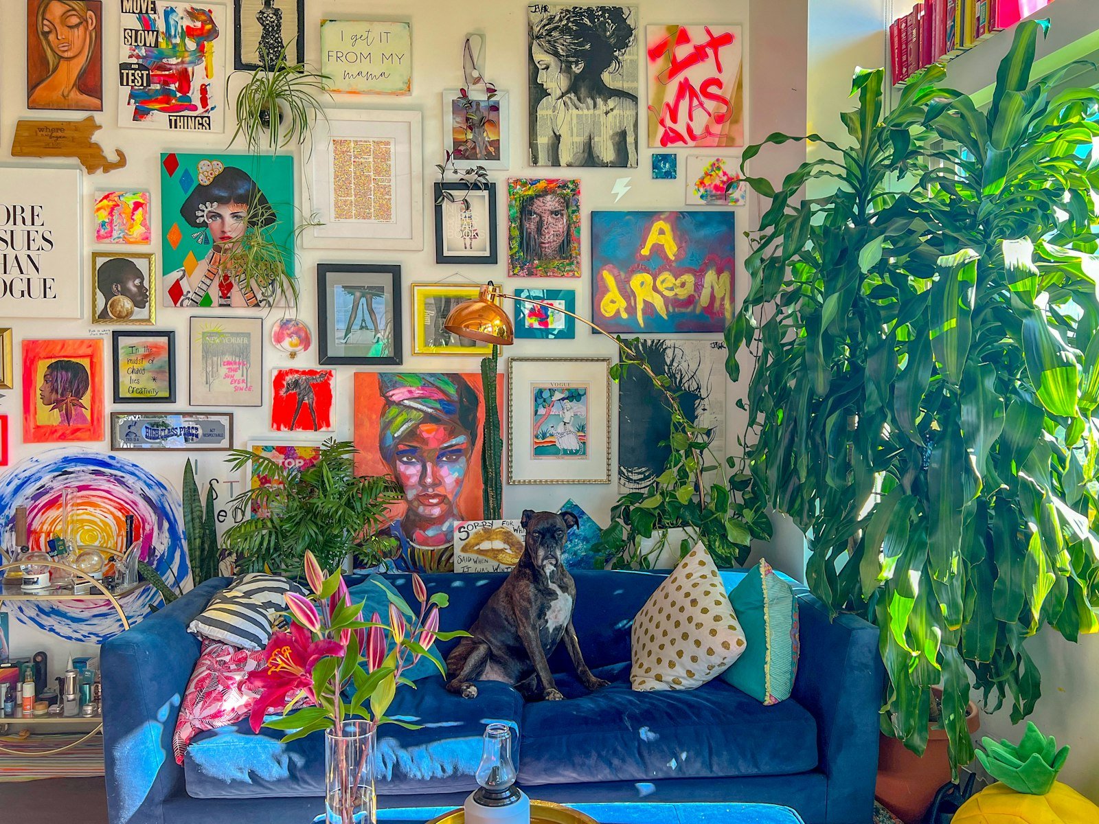 Living room with a blue sofa, a dense floor-to-ceiling gallery wall of colourful art and large leafy plants