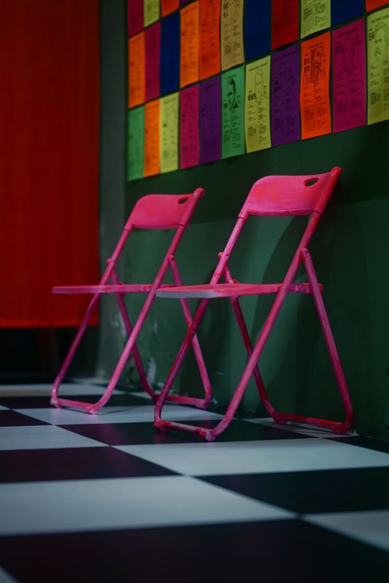 Two hot pink folding chairs on a black and white checkered floor against a dark green wall