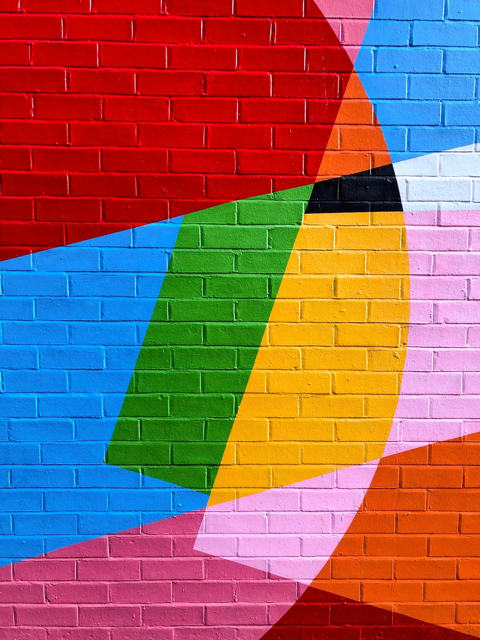 Brick wall painted with bold overlapping shapes in red, blue, green, yellow and pink