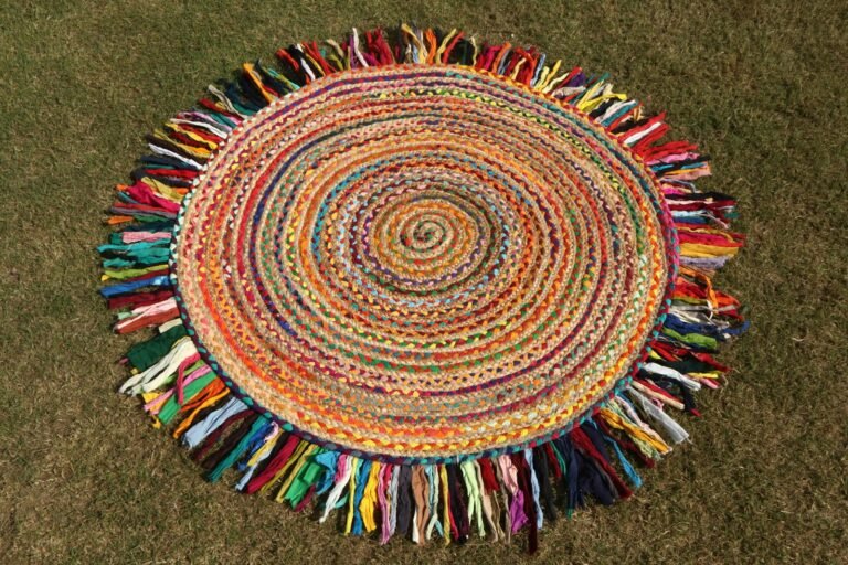 Round braided rug made of multicoloured fabric strips with a long rainbow fringe, lying on grass