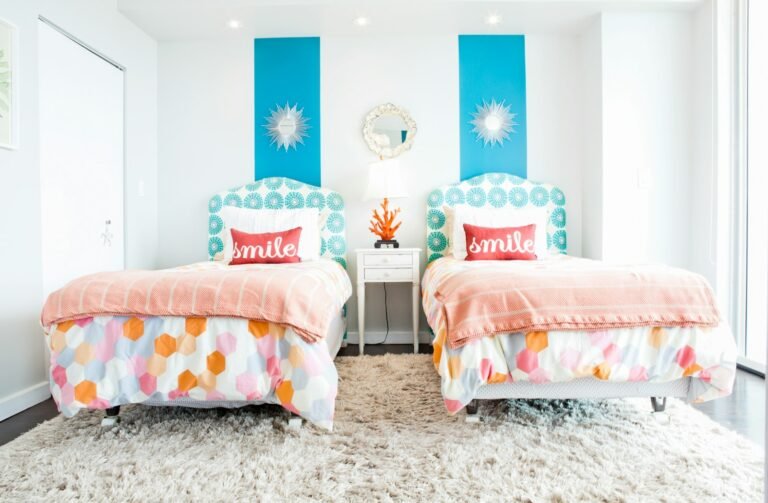 Twin beds with pink and multicoloured floral bedding, scalloped headboards and two turquoise sunburst prints on a white wall
